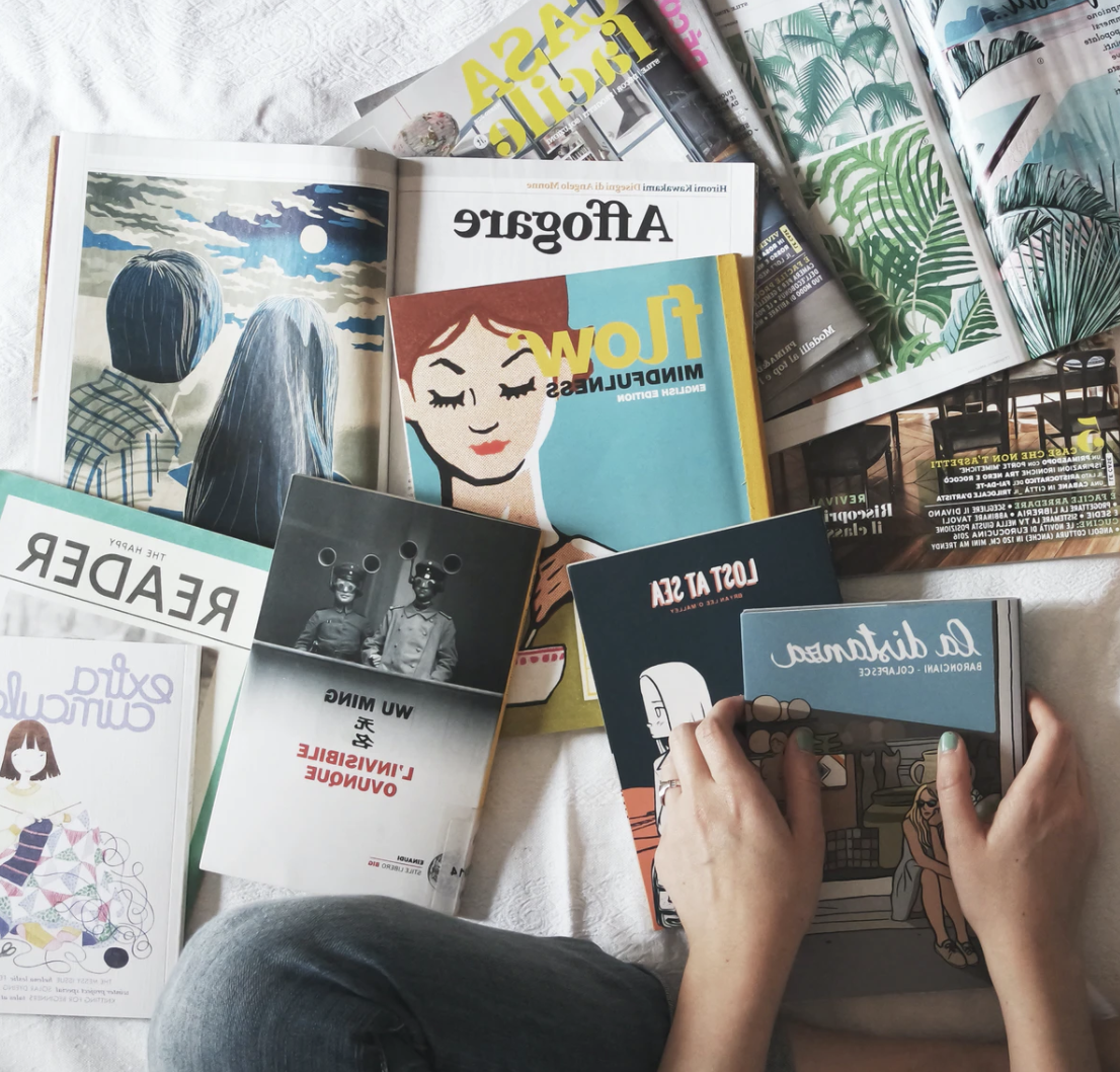 A small pile of scattered magazines on a bed.